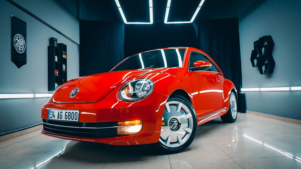Vibrant red Volkswagen Beetle parked in a sleek indoor showroom, showcasing its classic design. splash auto zone