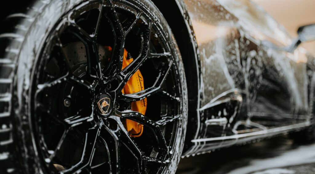 Detailed close-up of a luxury car wheel covered in soap suds during a professional car wash. splash auto zone