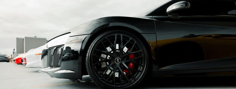 Close-up of a black luxury sports car's wheel detail in an outdoor setting. splash auto zone