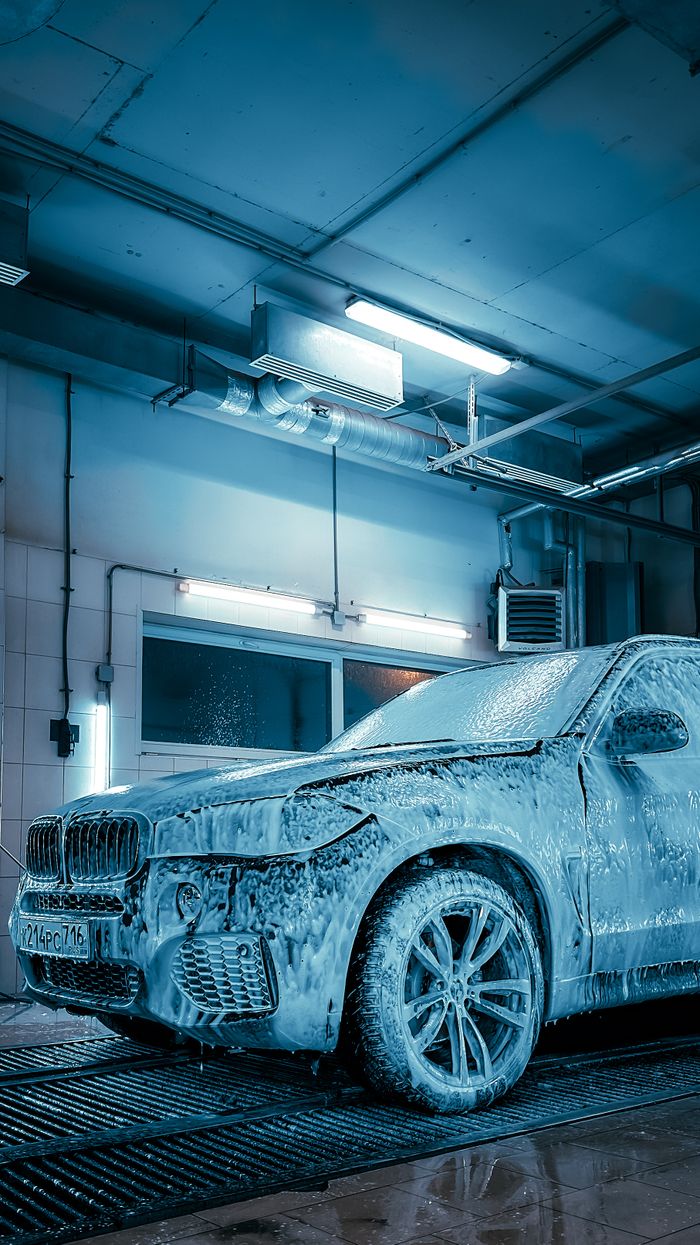 Luxury SUV covered in foam inside a modern car wash station enhanced by blue lighting. splash auto zone