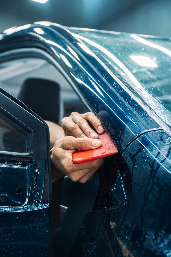 Close-up of a technician installing PPF on a car door in a workshop. splash auto zone