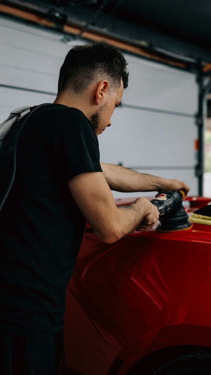 Young man using a polisher on a shiny red car in a garage setting. splash auto zone