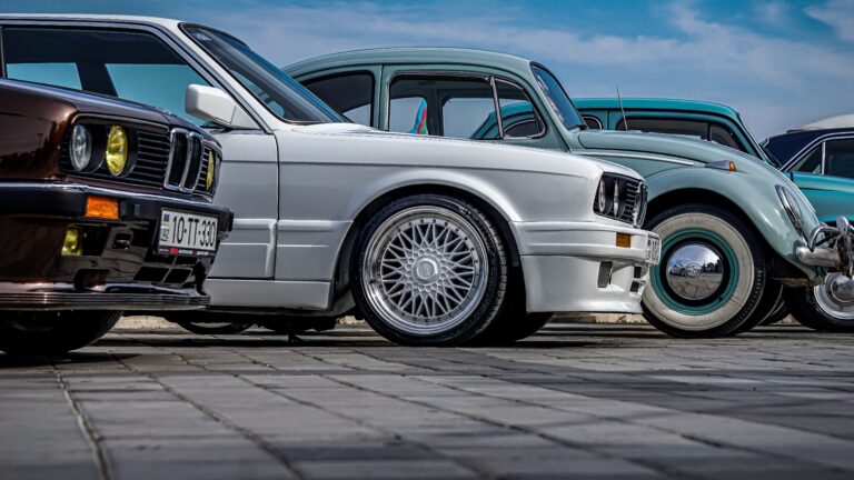 A lineup of vintage cars including a BMW and Volkswagen Beetle showcased outdoors on a sunny day.