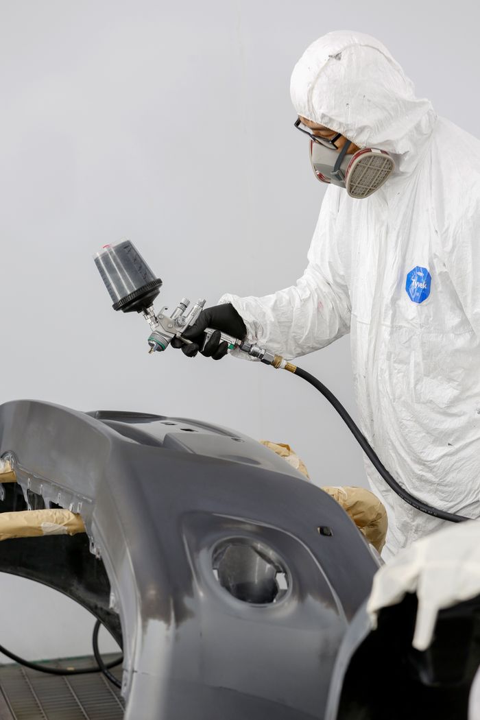 Technician in protective gear spray painting a car bumper. splash auto zone car washing and detailing car wash abu dhabi