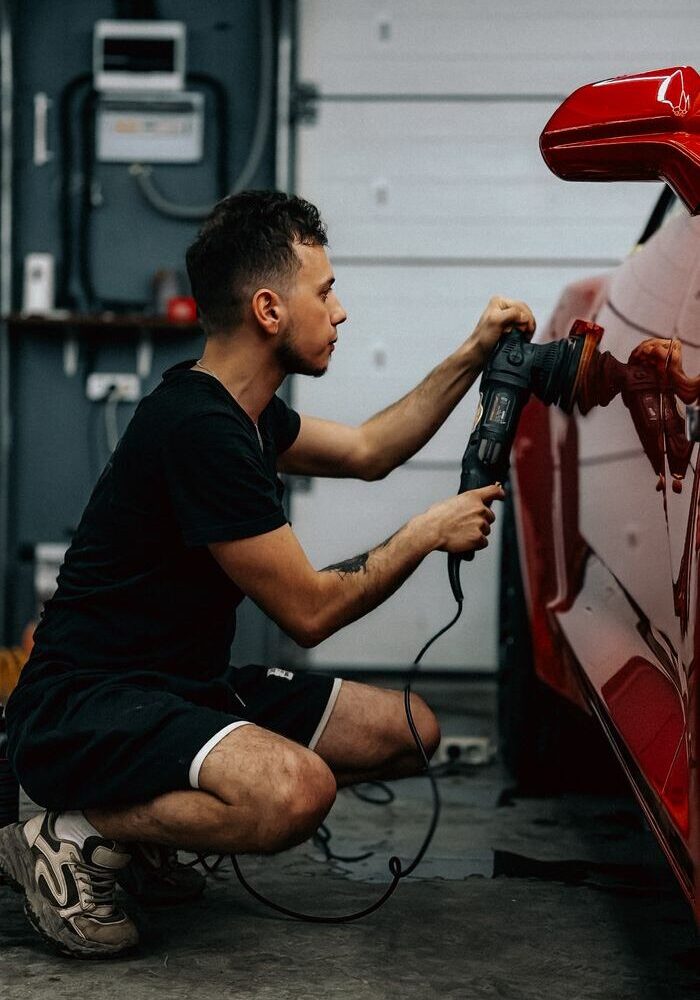 Man polishing a red sports car in a garage setting, demonstrating car detailing.